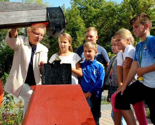 Die HistoryKids werden am 21. September zwei Jahre alt. Vor kurzem trafen sie sich am Alten Schmiedehammer vor der Bibliothek. Hier ließen sich die geschichtsinteressierten Kinder von Helga Ass diesen speziellen Typ Schwanzhammer erklären, an dem sie in der Messerschmiede viele Jahre gearbeitet hatte. (Foto: Liane Protzmann)